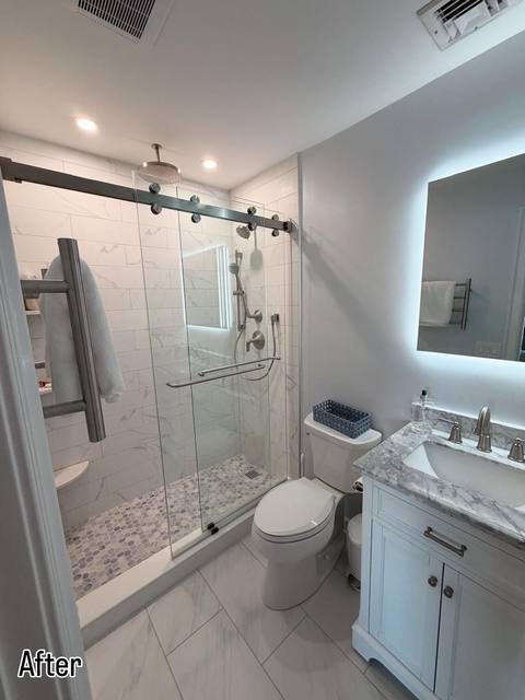 Remodeled bathroom with marble-look tile shower and glass sliding door
