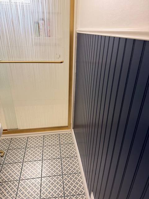 Close-up of gold shower door trim against navy beadboard wall
