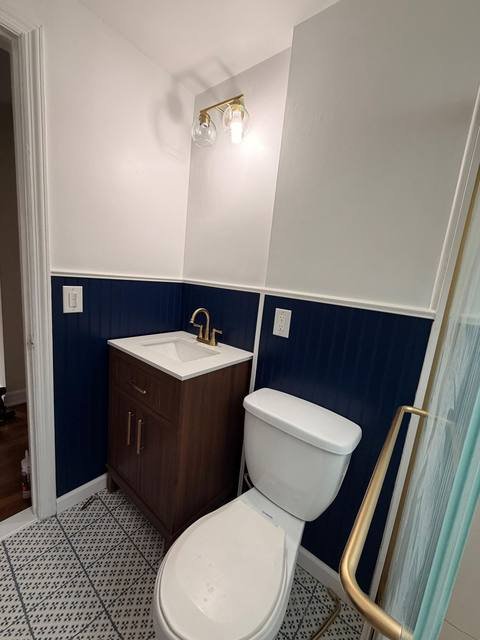 Navy blue bathroom vanity and toilet with brushed gold sconce light